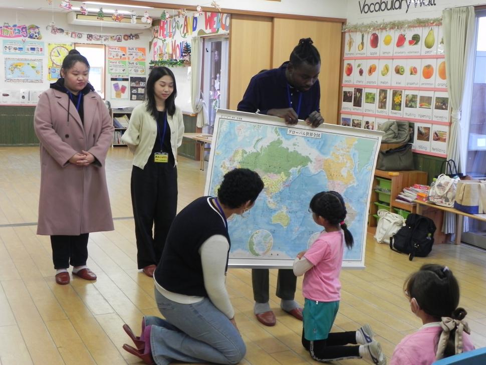 世界地図を見ながら留学生と話す園児